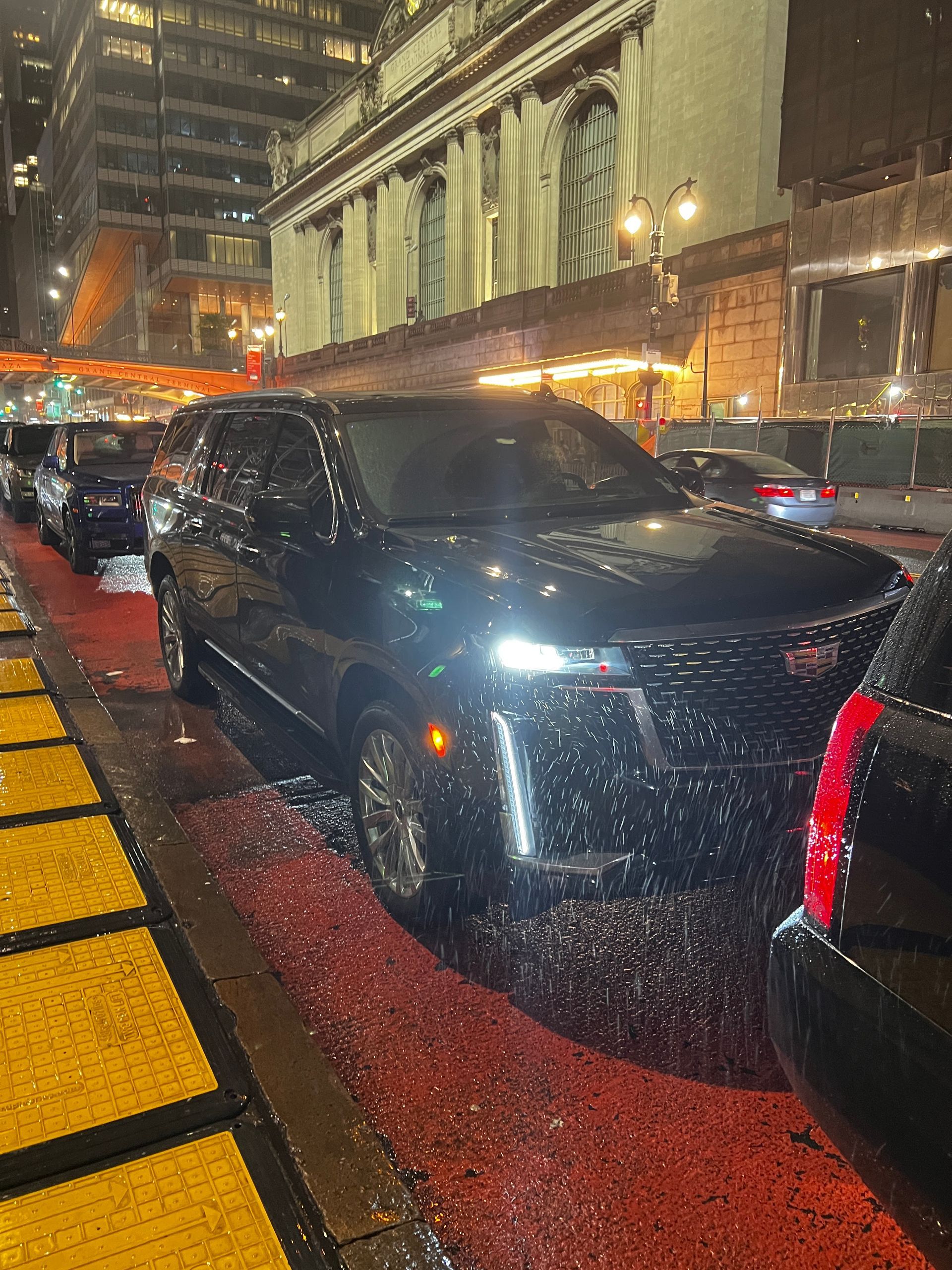 A black cadillac is parked on a city street at night