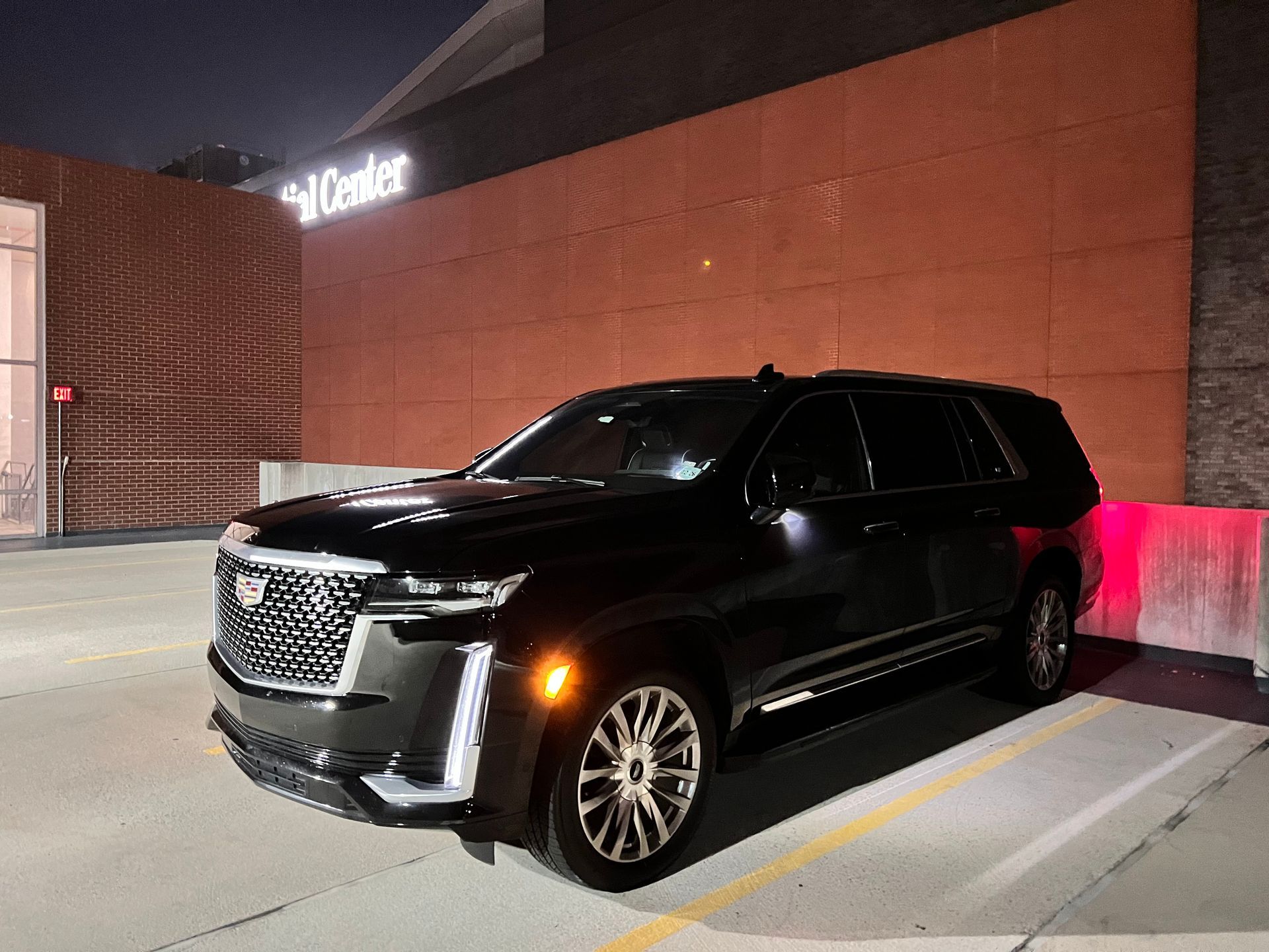 A black cadillac escalade is parked in a parking lot at night.