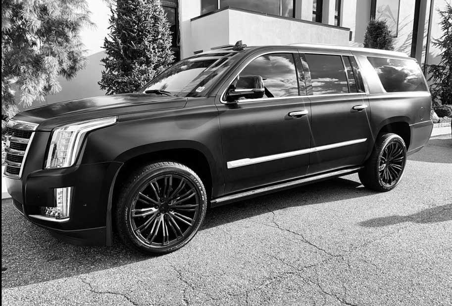 A black and white photo of a cadillac escalade parked in front of a building.