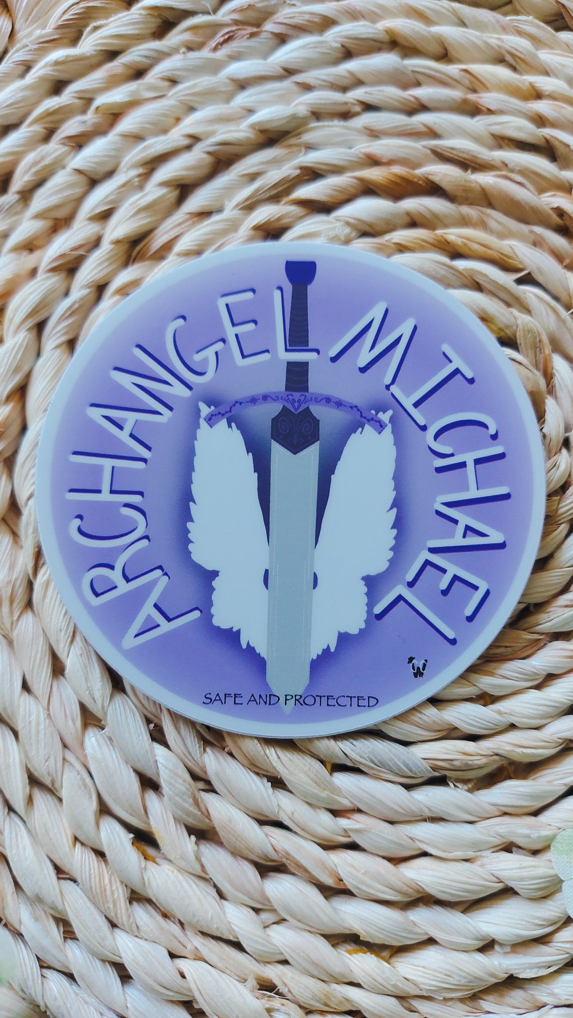 A purple archangel michael sticker is sitting on top of a wicker mat.