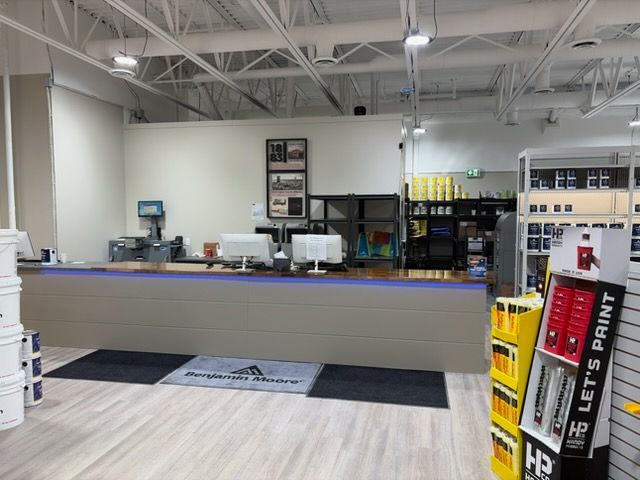 A light-filled store interior with a counter, display shelves, and paint cans. A person is not visible.