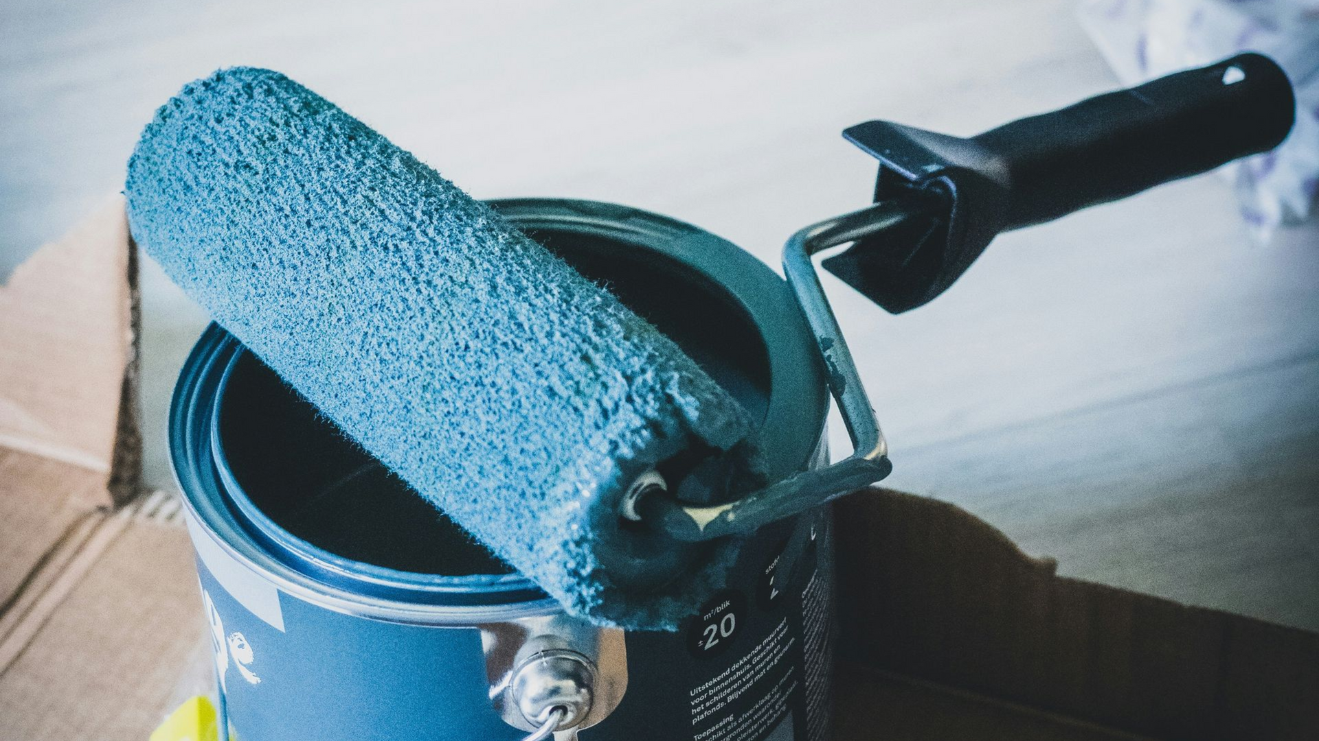 Paint roller resting on an open can of blue paint.
