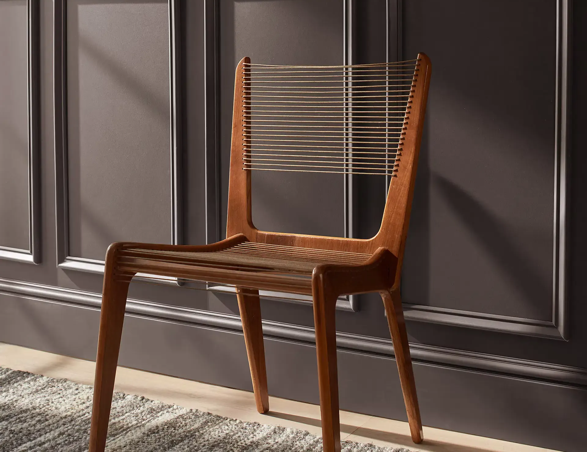 Wooden chair with woven seat and back, against a gray wall.