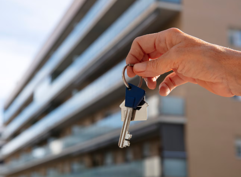 Mano sosteniendo llaves frente a un moderno edificio de apartamentos.