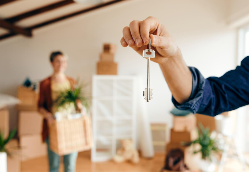 Mano sosteniendo una llave frente a una persona con cajas, posiblemente mudándose a una nueva casa.