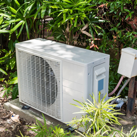 Outdoor air conditioner unit beside lush green plants and a white utility box