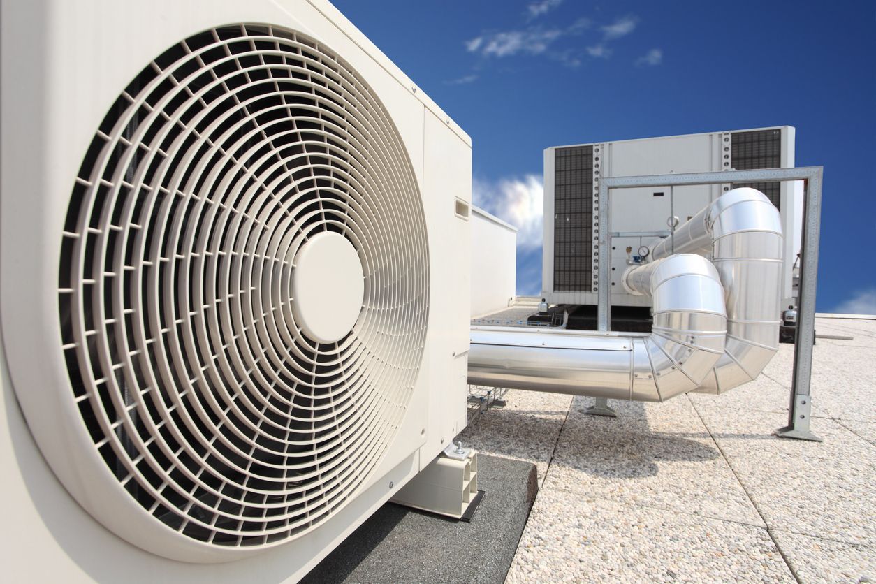 Rooftop HVAC units with large circular fan, ducts, and metal vents under a blue sky.