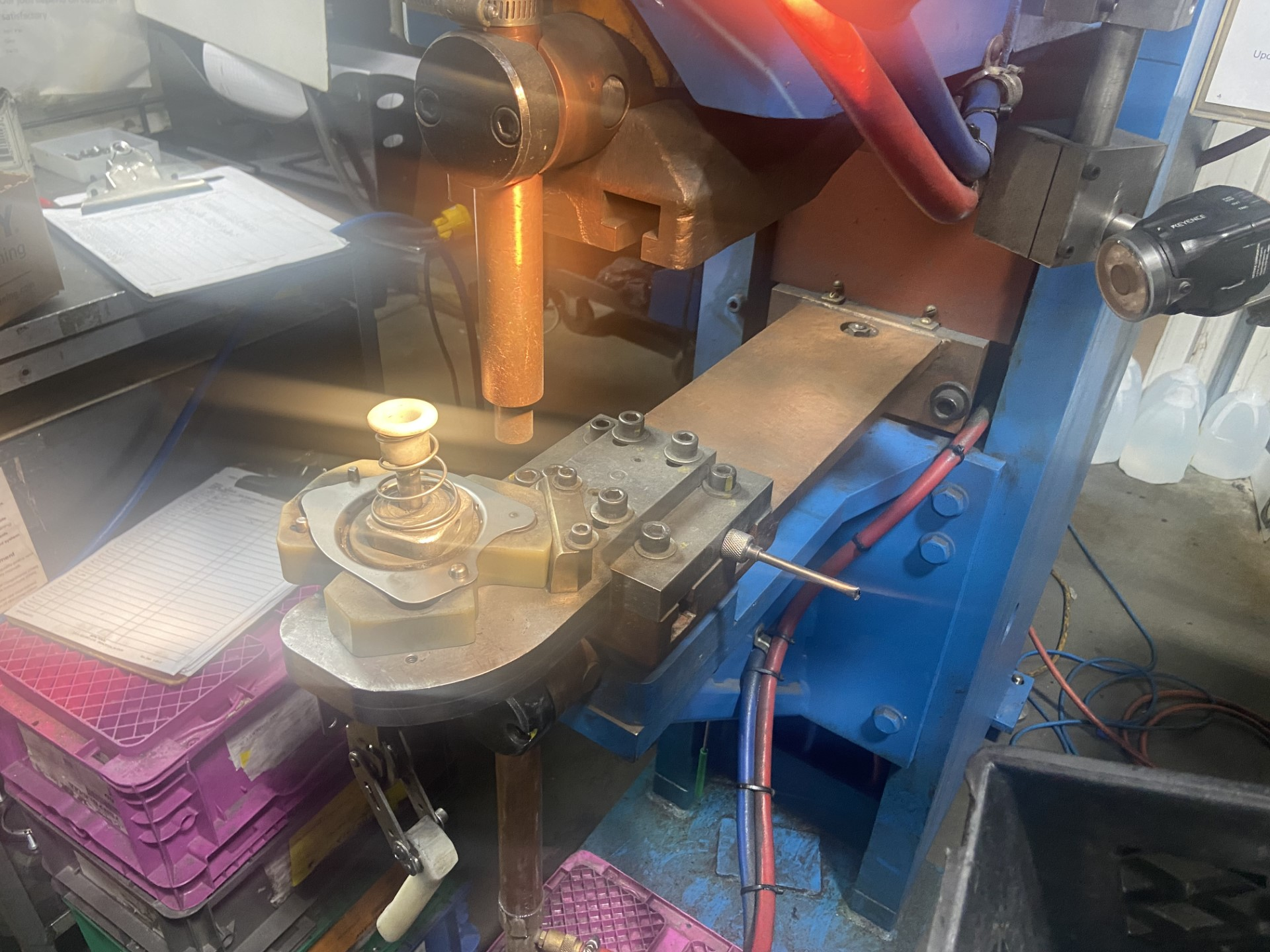 Spot welding machine, copper electrodes, blue and red tubes, metal parts, industrial setting.