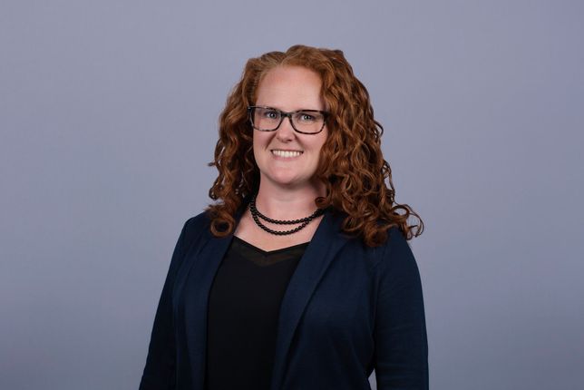 Woman with red hair and glasses smiling against a blue background.