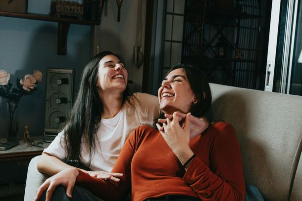 Two women are sitting on a couch laughing together.