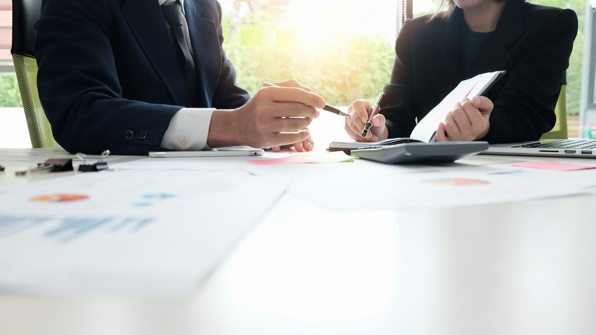 A man is sitting at a table using a calculator and a pen.