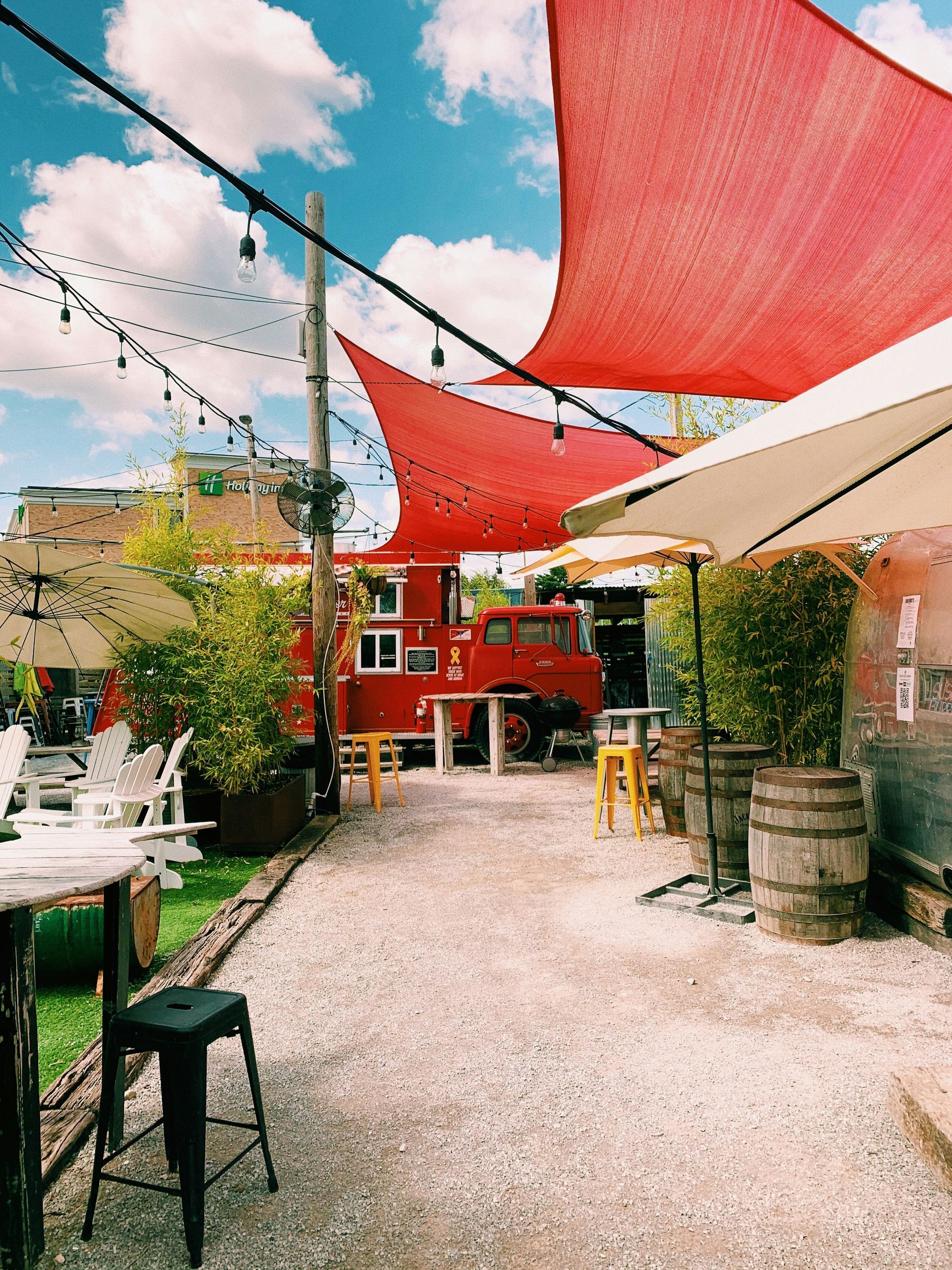 A red fire truck is parked in the backyard of a restaurant with tables and umbrellas.