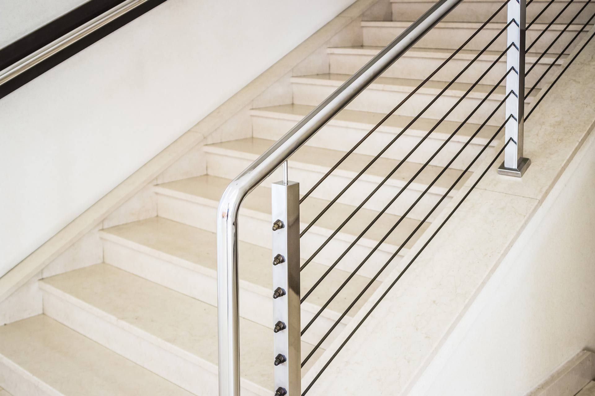 Staircase with light stone steps and metal railing with horizontal black bars.