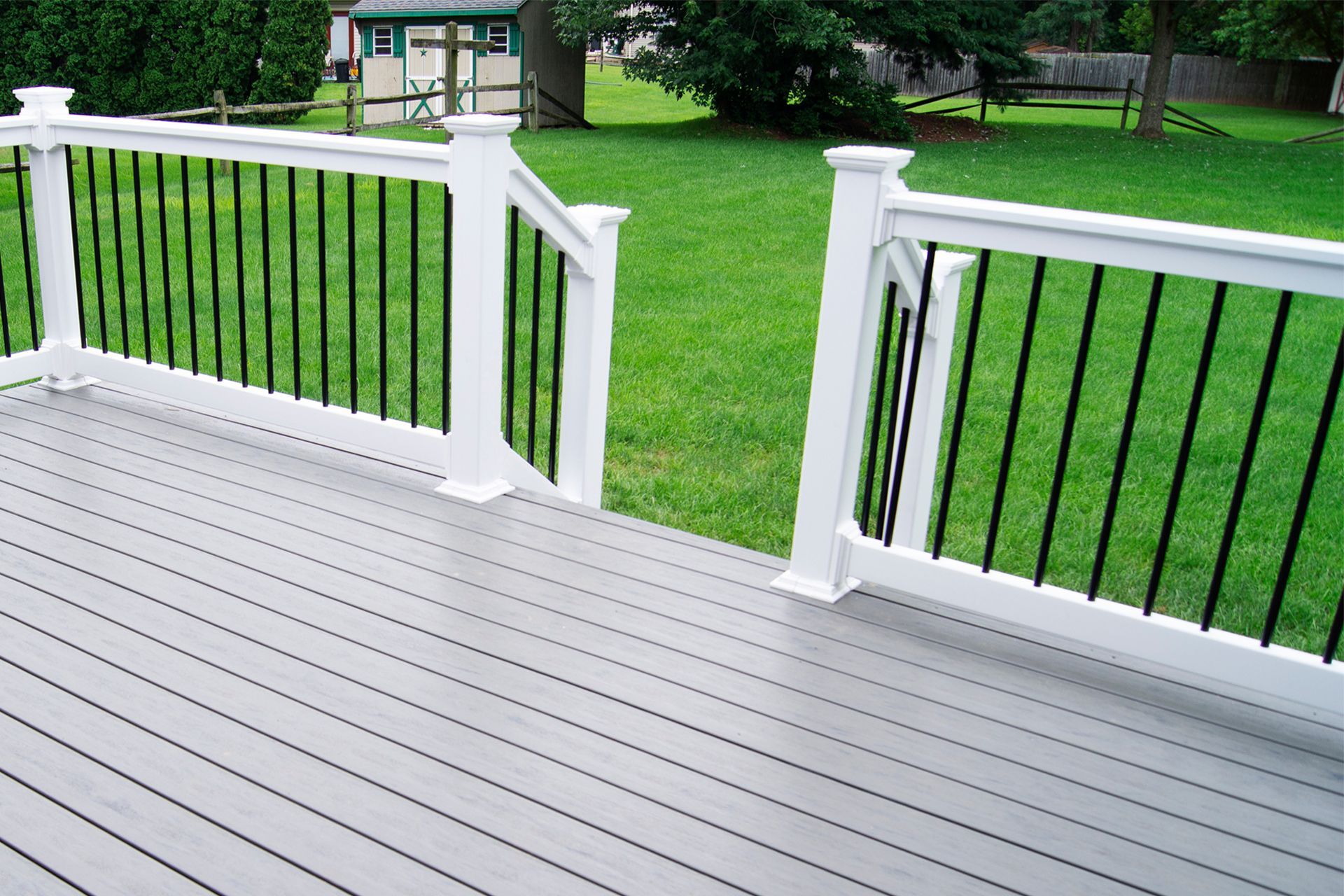 Gray composite deck with white railings and black balusters, overlooking a grassy yard.