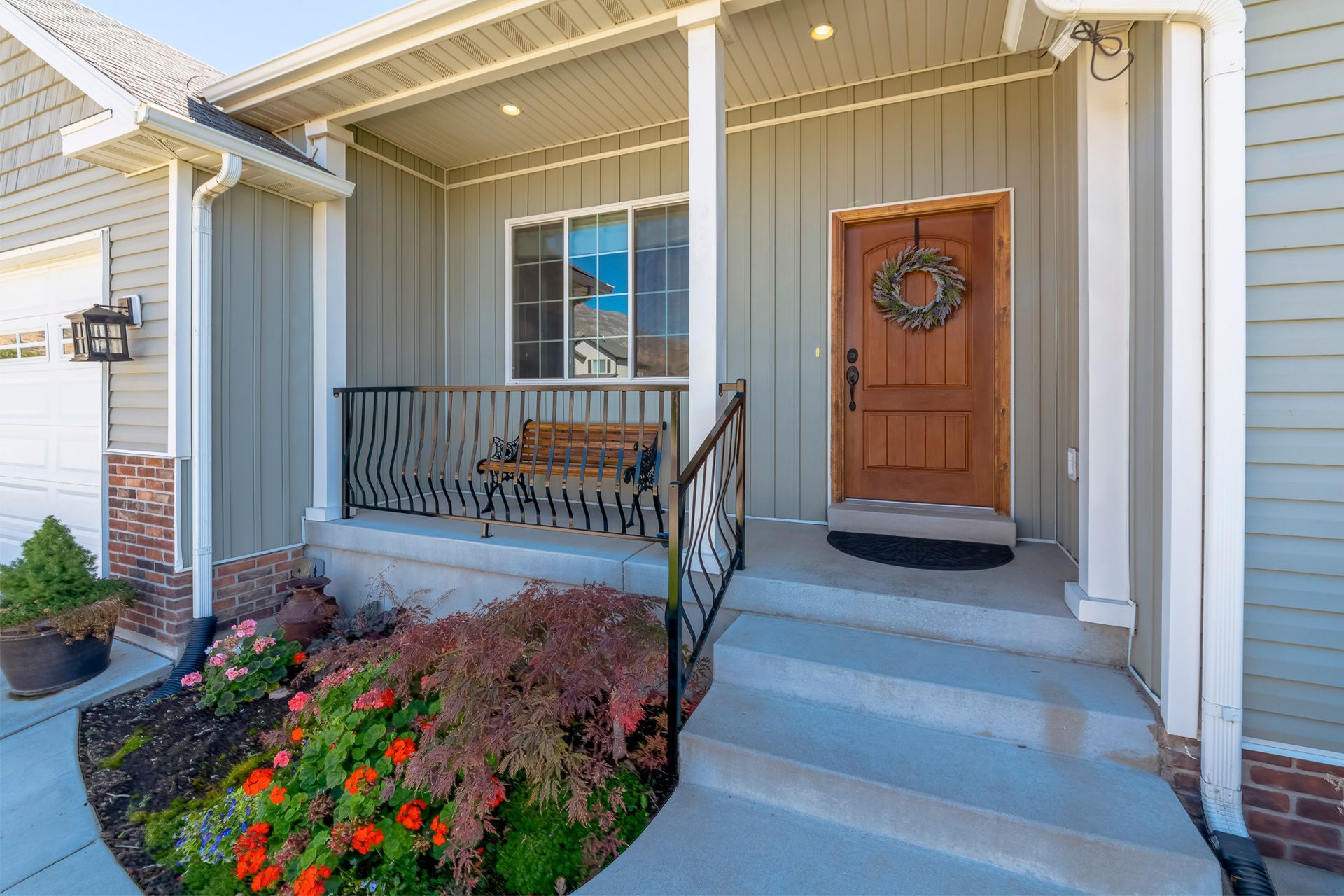 Exterior of a house with a porch. Steps lead up to a brown door with a wreath. A bench sits beside a window.