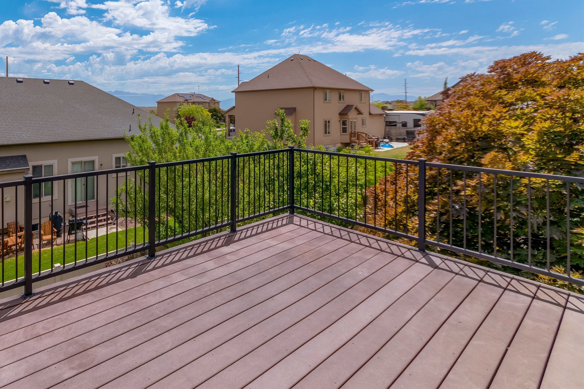 Deck with brown composite flooring and black railing overlooking a neighborhood.