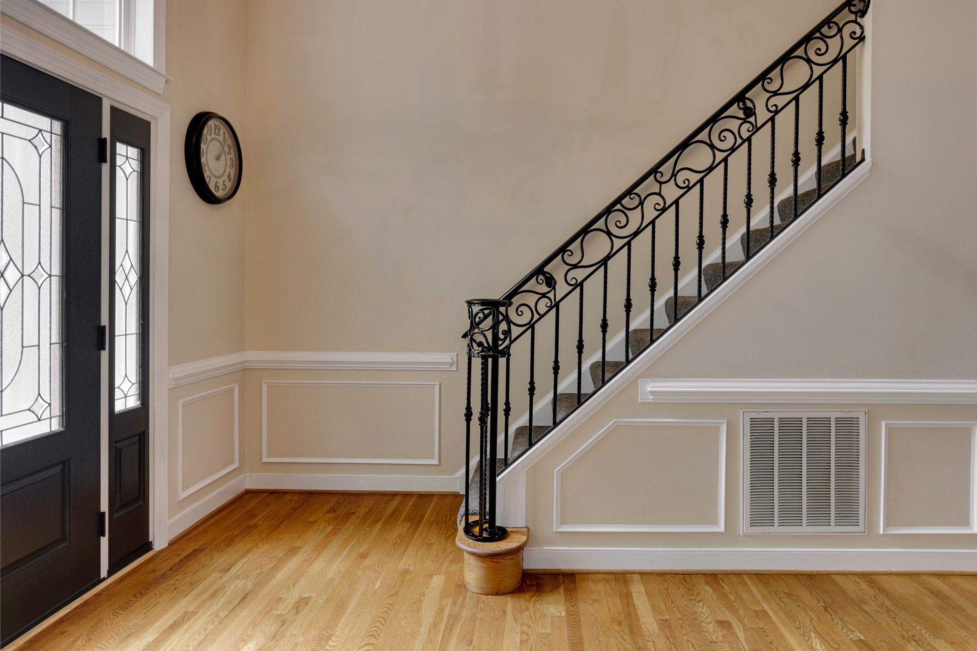 Entryway with staircase, black door, and decorative molding on beige walls.
