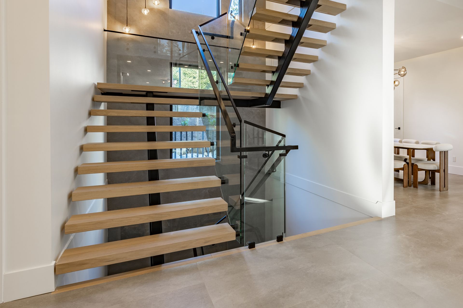 Modern staircase with wooden steps, glass railing, and black metal frame in a bright home.