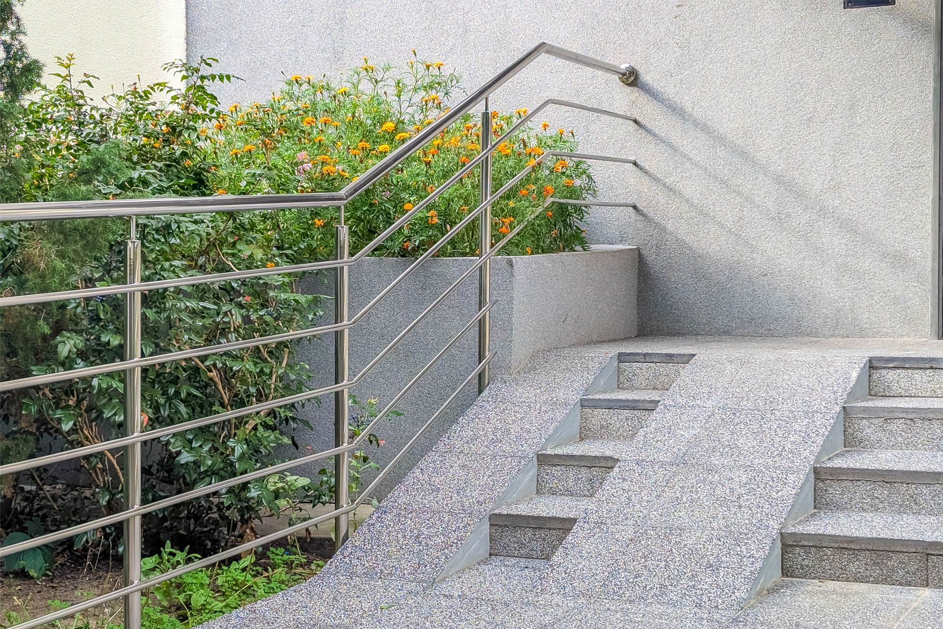 Steps leading to a building with a textured facade and stainless steel railing.