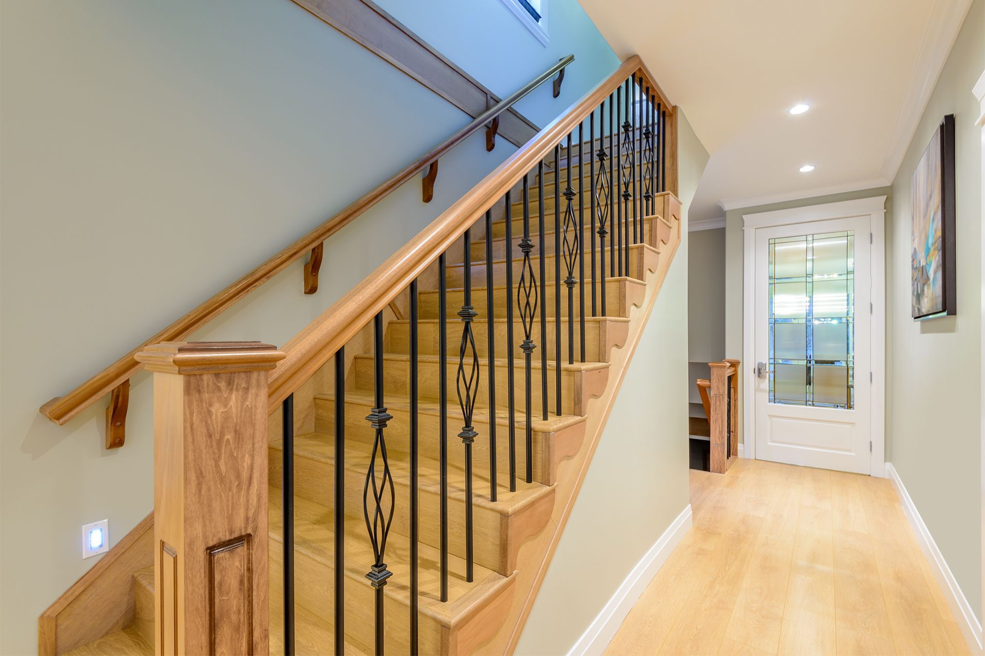 Wooden staircase with black metal balusters, leading up to a hallway with a white door.