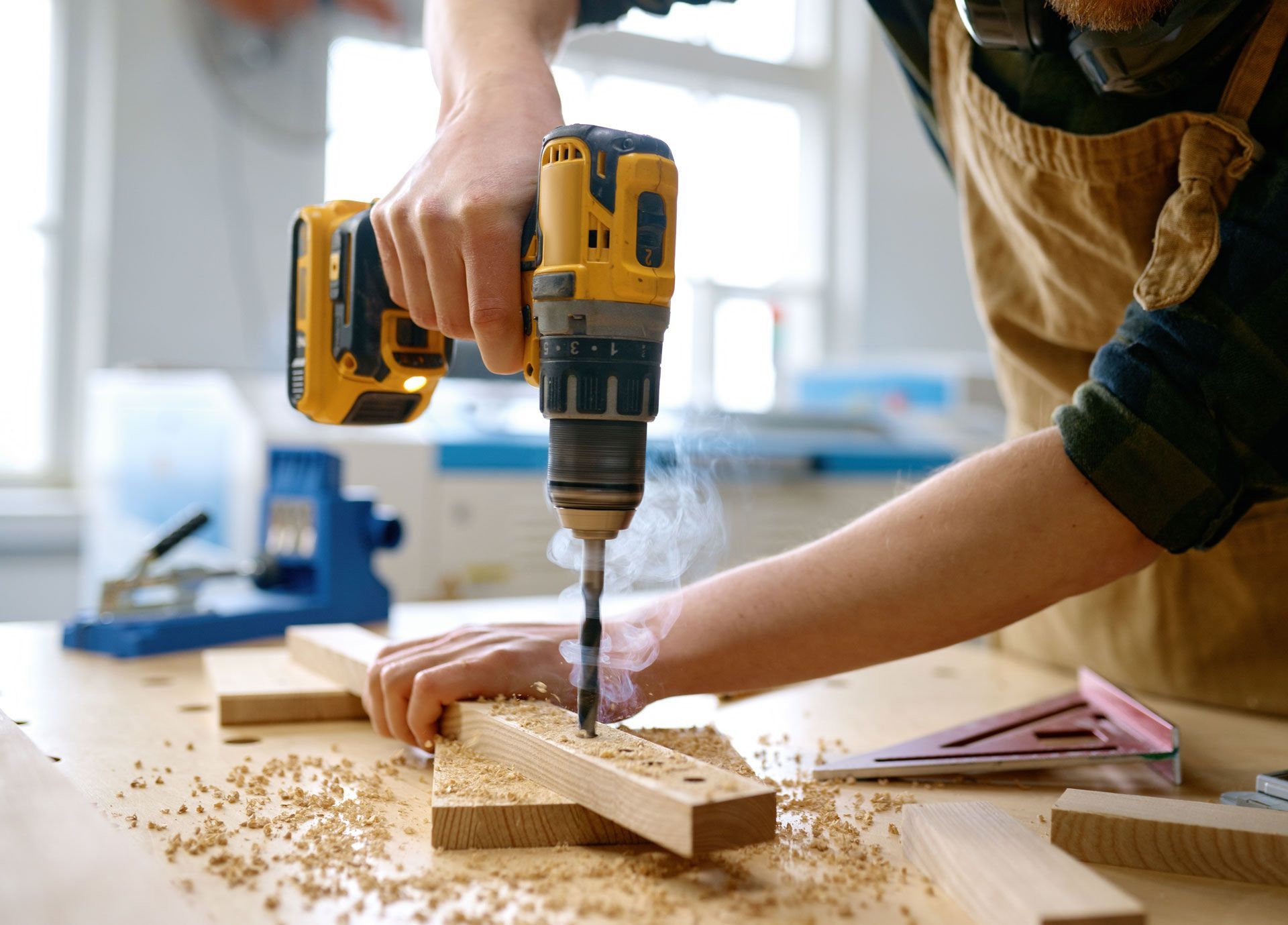 Hands drilling wood on a workbench with a yellow power drill and sawdust scattered շուրջ