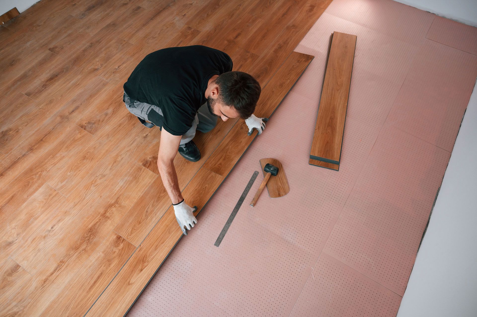 Person installing wood flooring with a hammer and tools on a pink subfloor