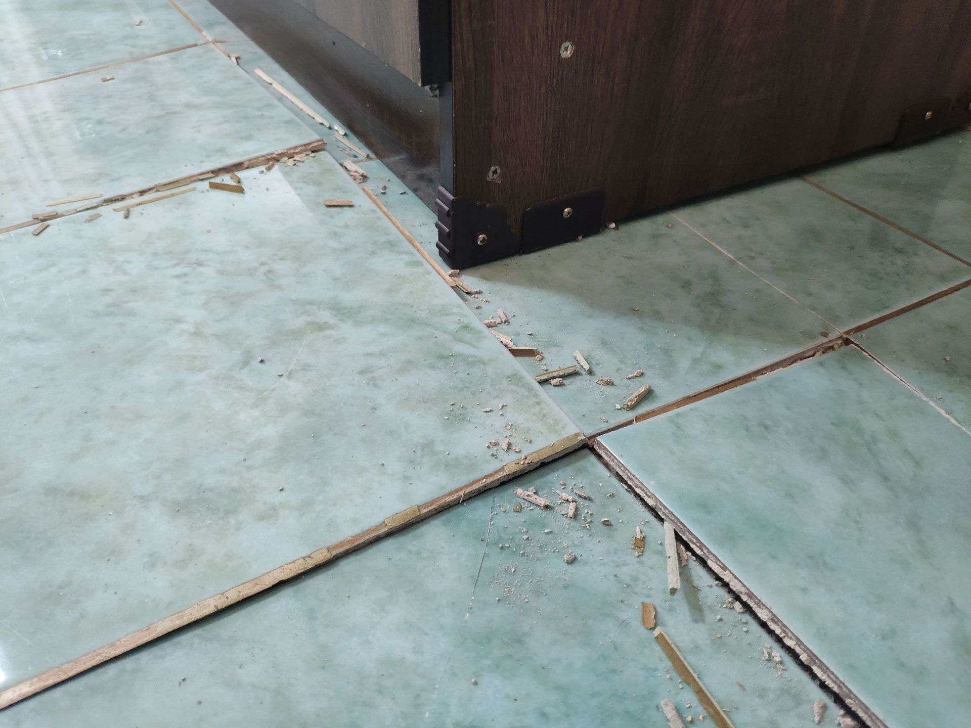 Cracked pale blue tile floor beside a dark wooden cabinet corner