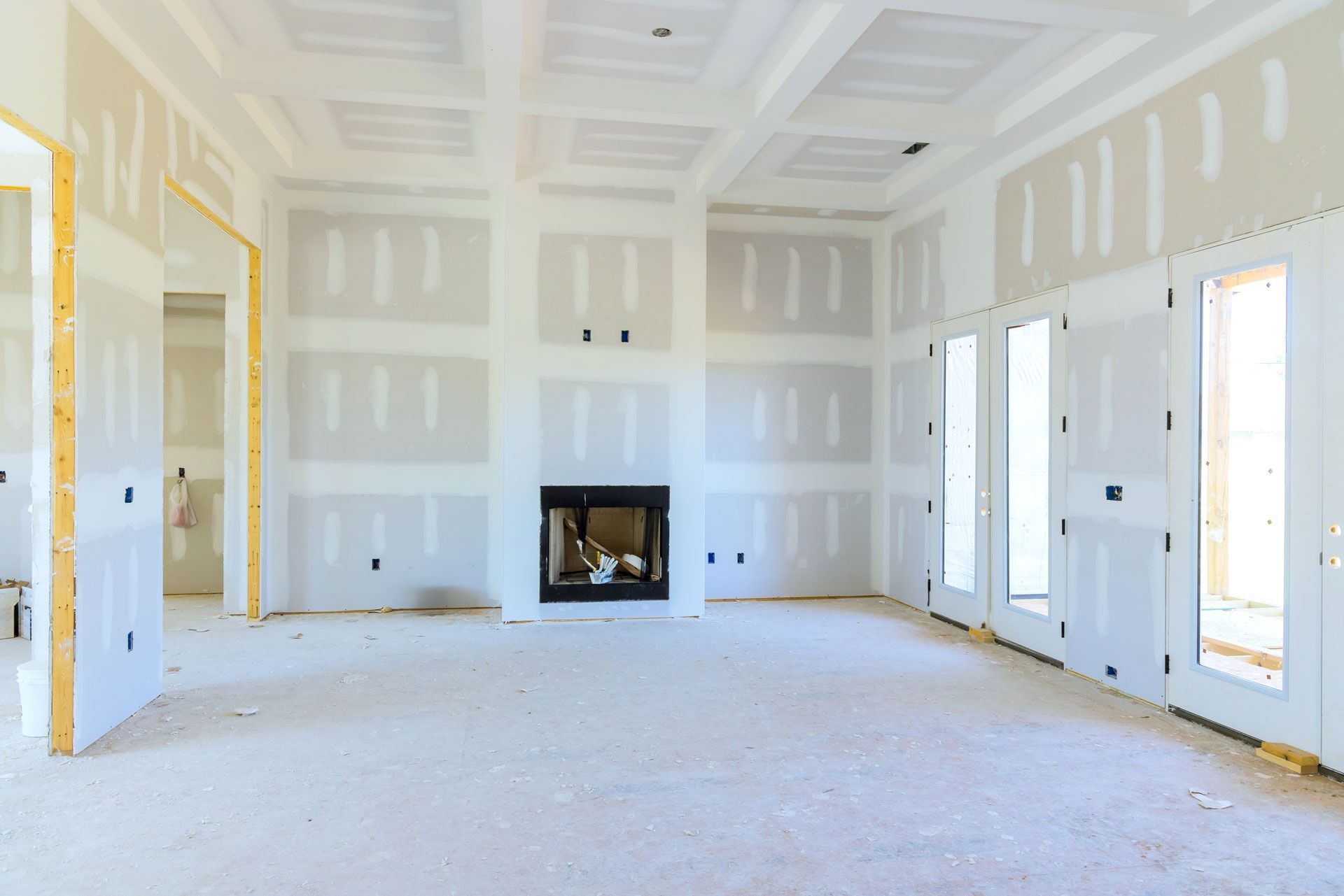 Bright unfinished room with white drywall, fireplace, and large windows receiving daylight
