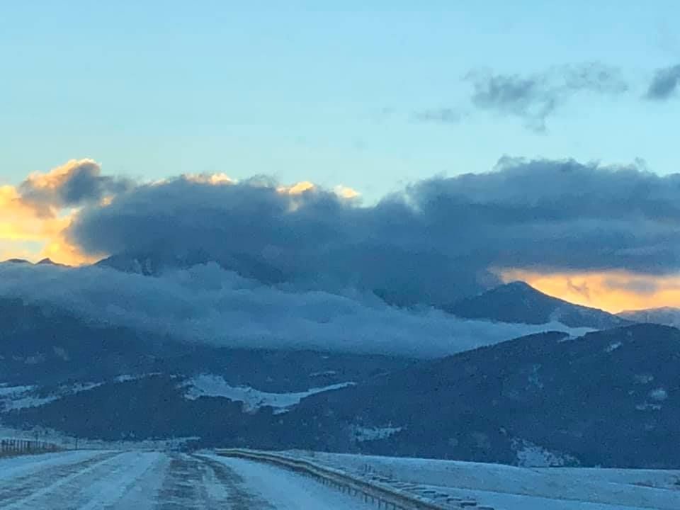 A snowy road with mountains in the background and clouds in the sky