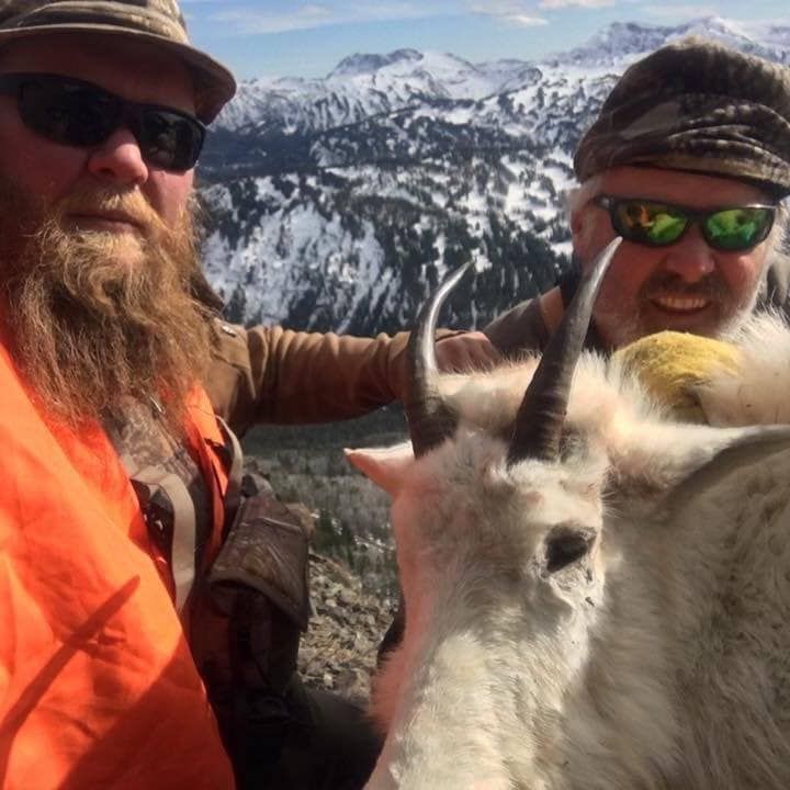 Two men are posing for a picture with a mountain goat