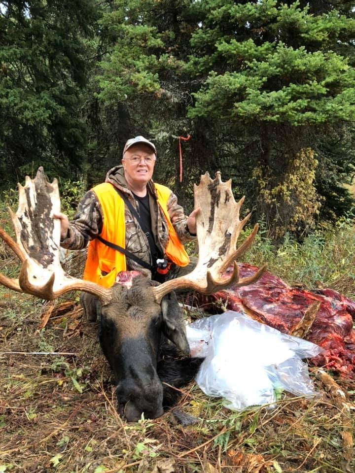 A man is standing next to a moose in the woods.