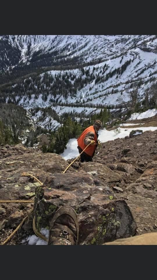 A person is climbing up a rocky mountain with a rope.