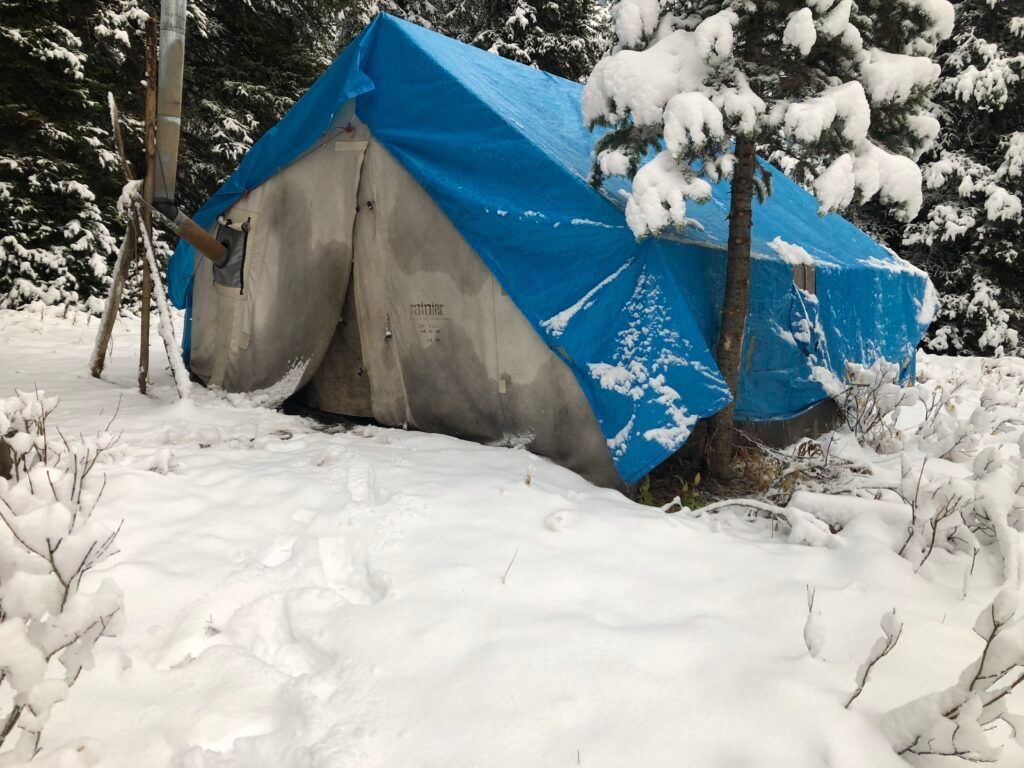 A blue tarp is covering a tent in the snow