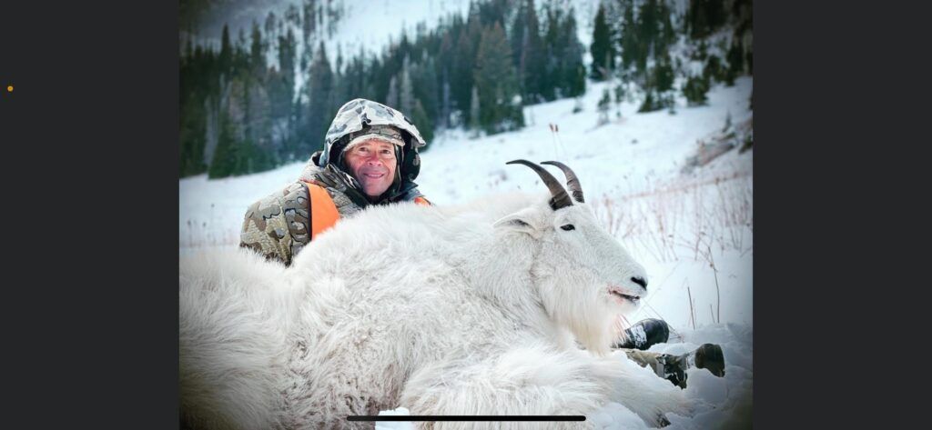 A man is standing next to a mountain goat in the snow.