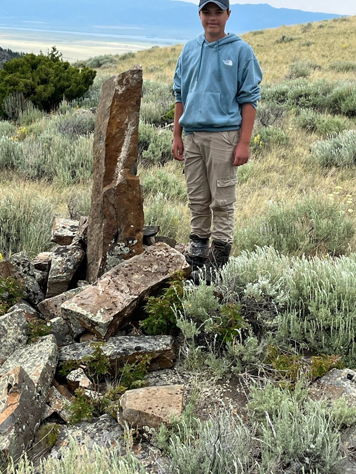 A man in a blue hoodie is standing next to a pile of rocks in a field.