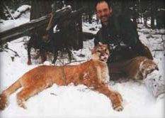 A man is standing next to a mountain lion in the snow.