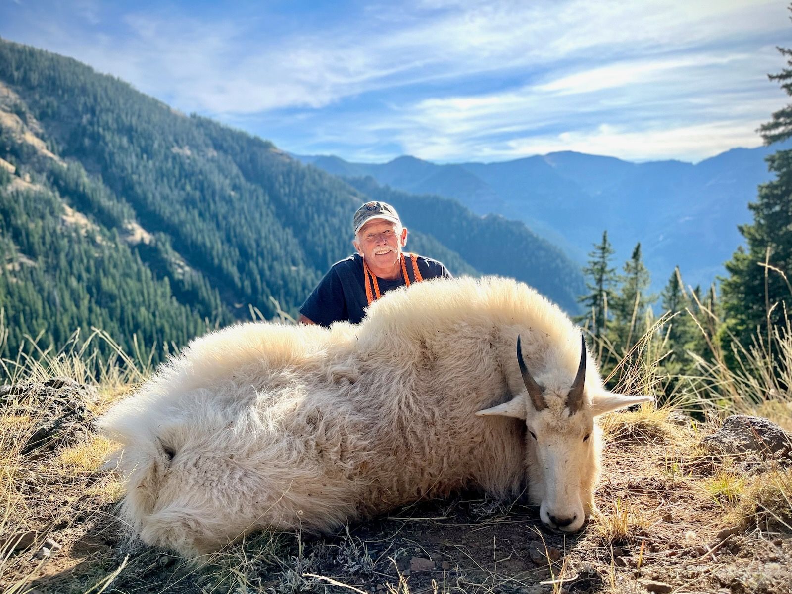 A man is standing next to a mountain goat on top of a hill.