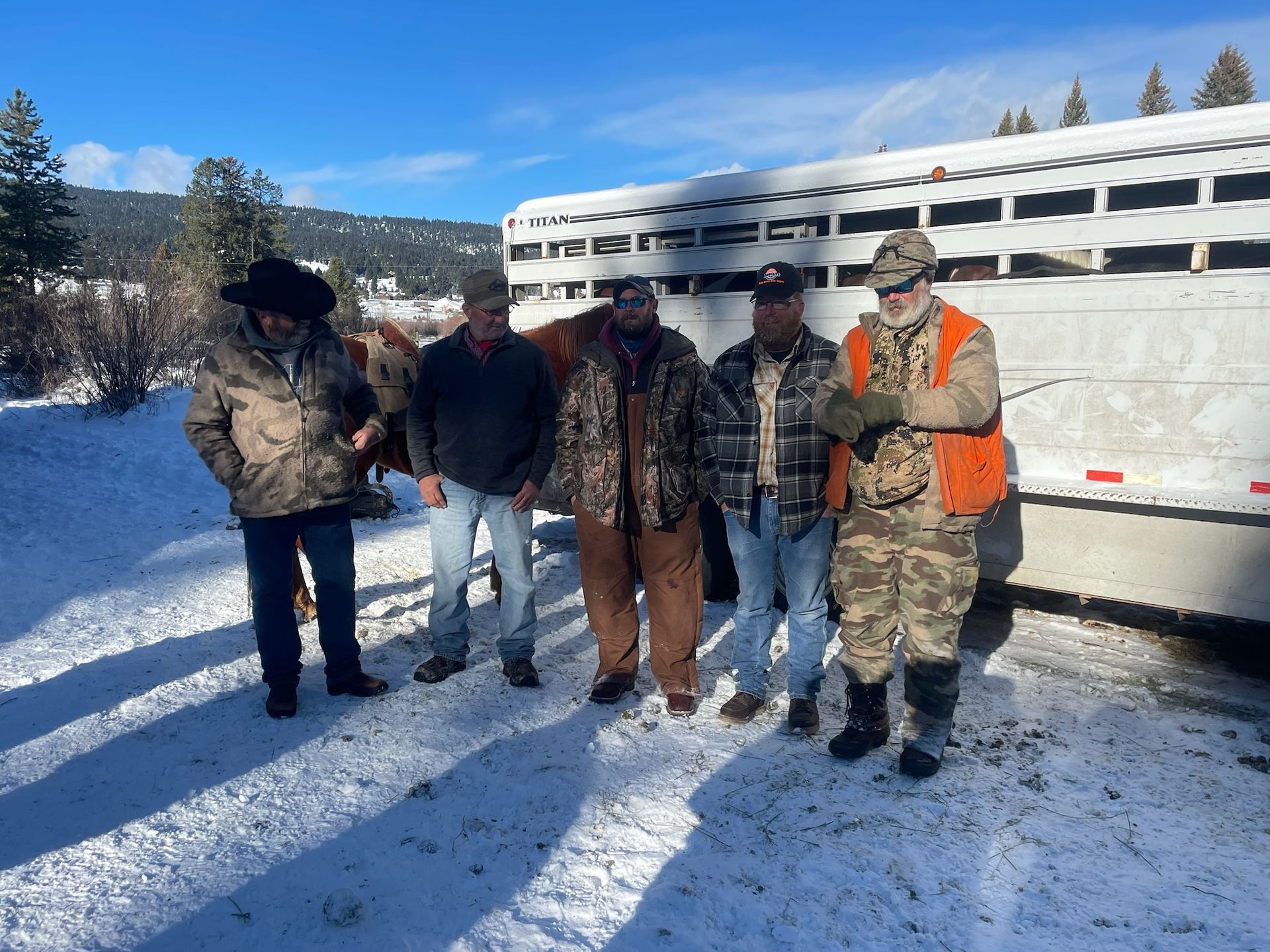 A group of men standing in the snow in front of a trailer