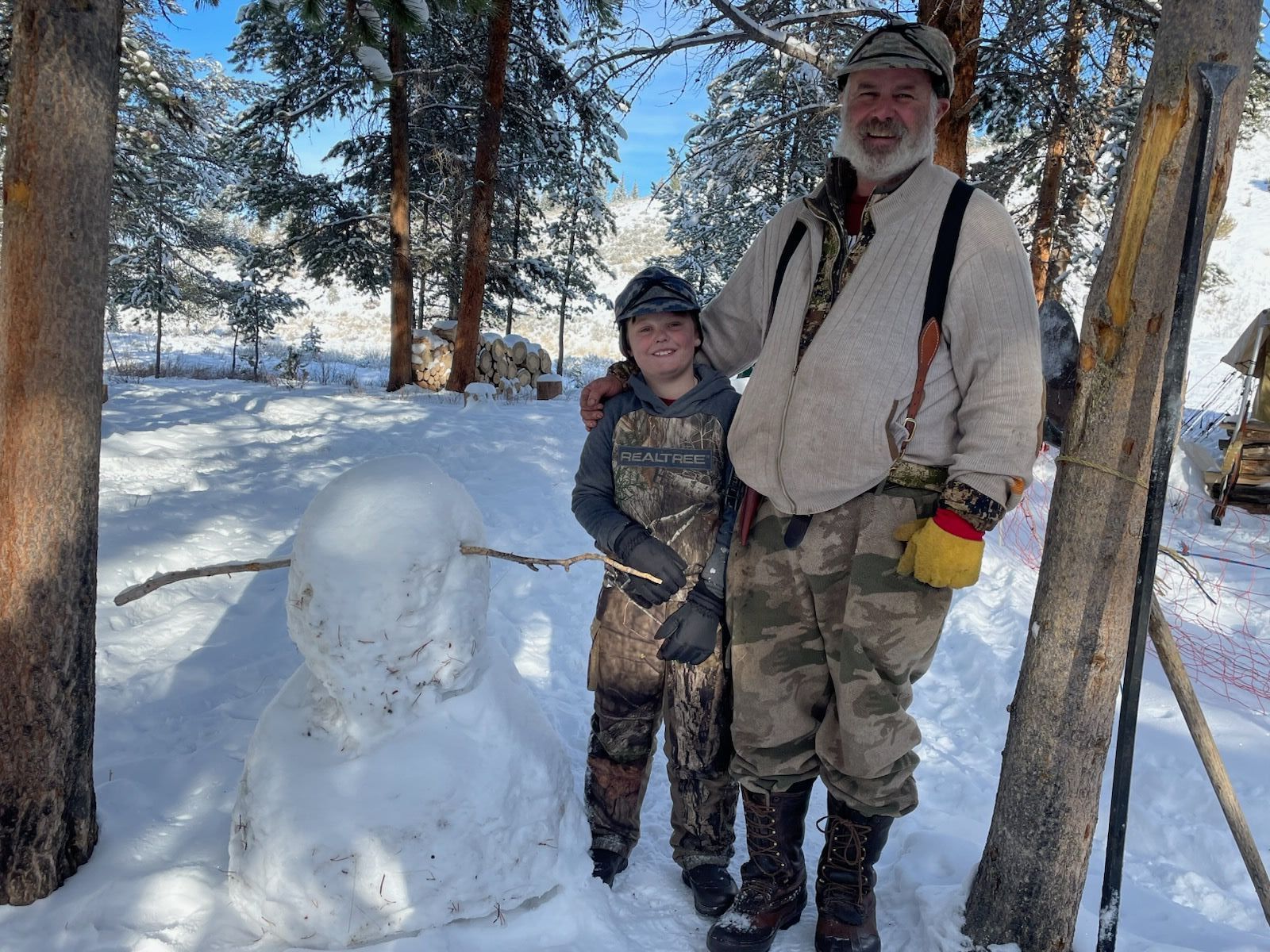A man and a boy are standing next to a snowman in the snow.