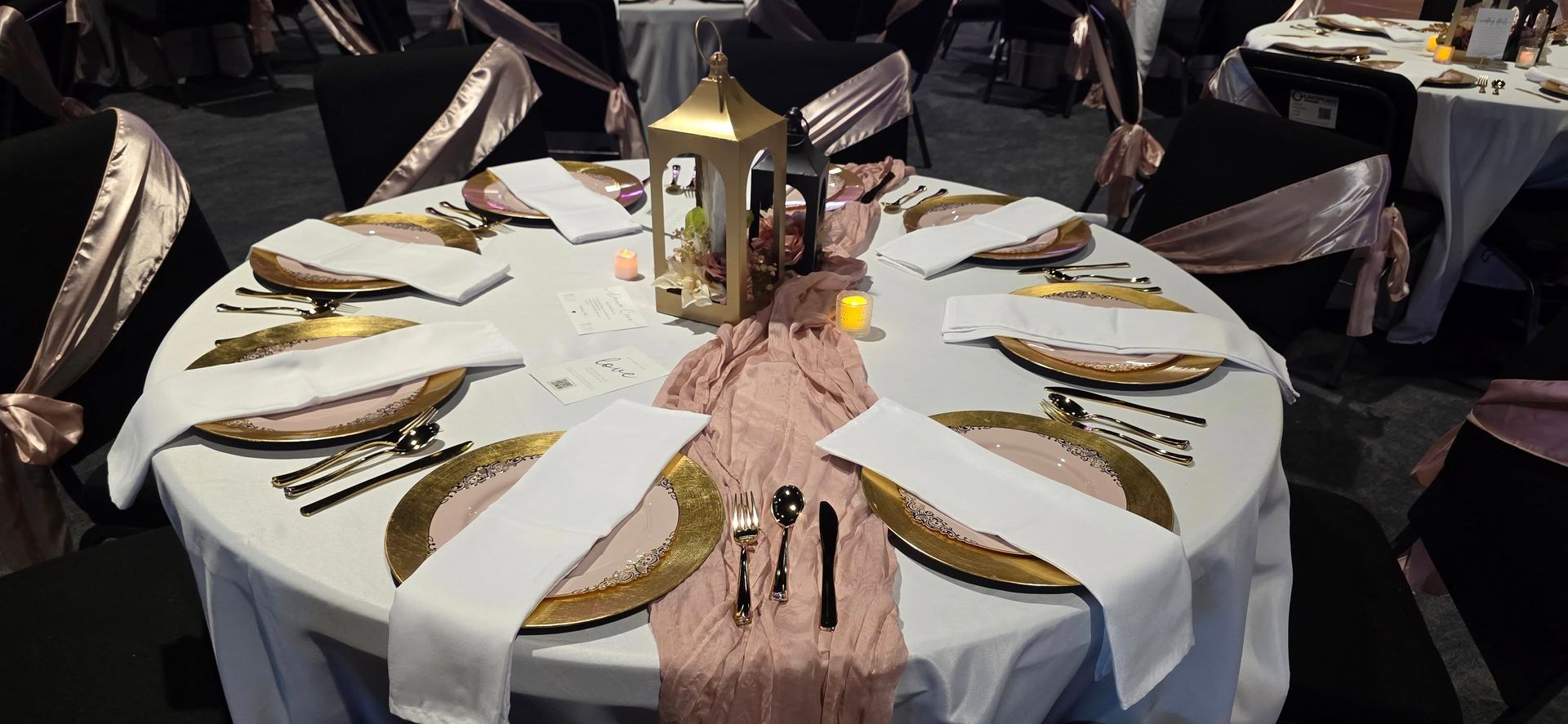 A table set for a formal event with gold chargers, white napkins, and pink accents.