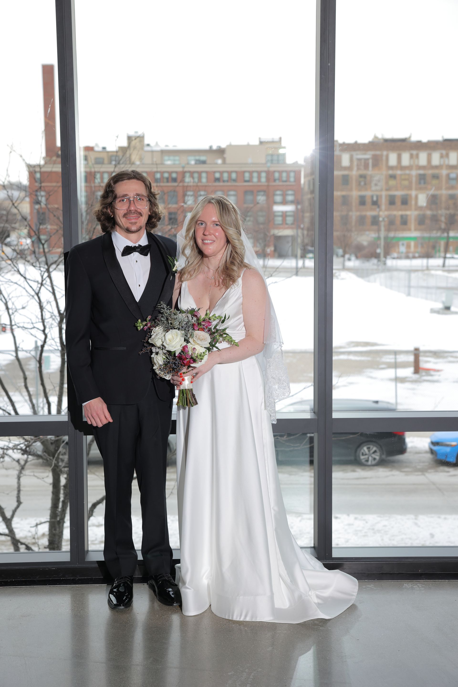 A newlywed couple poses in front of a window; bride in a white gown and holding a bouquet, groom in a black tuxedo.
With Love, Wedding management, Milwaukee Wedding Coordinator