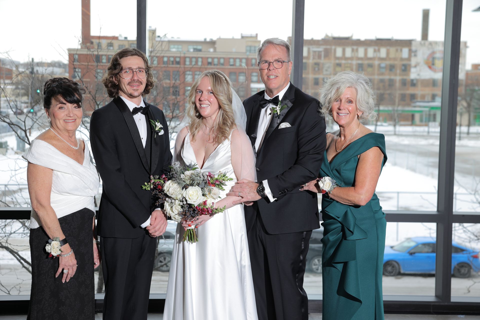 Wedding group poses by large window overlooking a city. Bride and groom stand with parents, all formal attire.
With Love, Wedding management, Milwaukee Wedding Coordinator