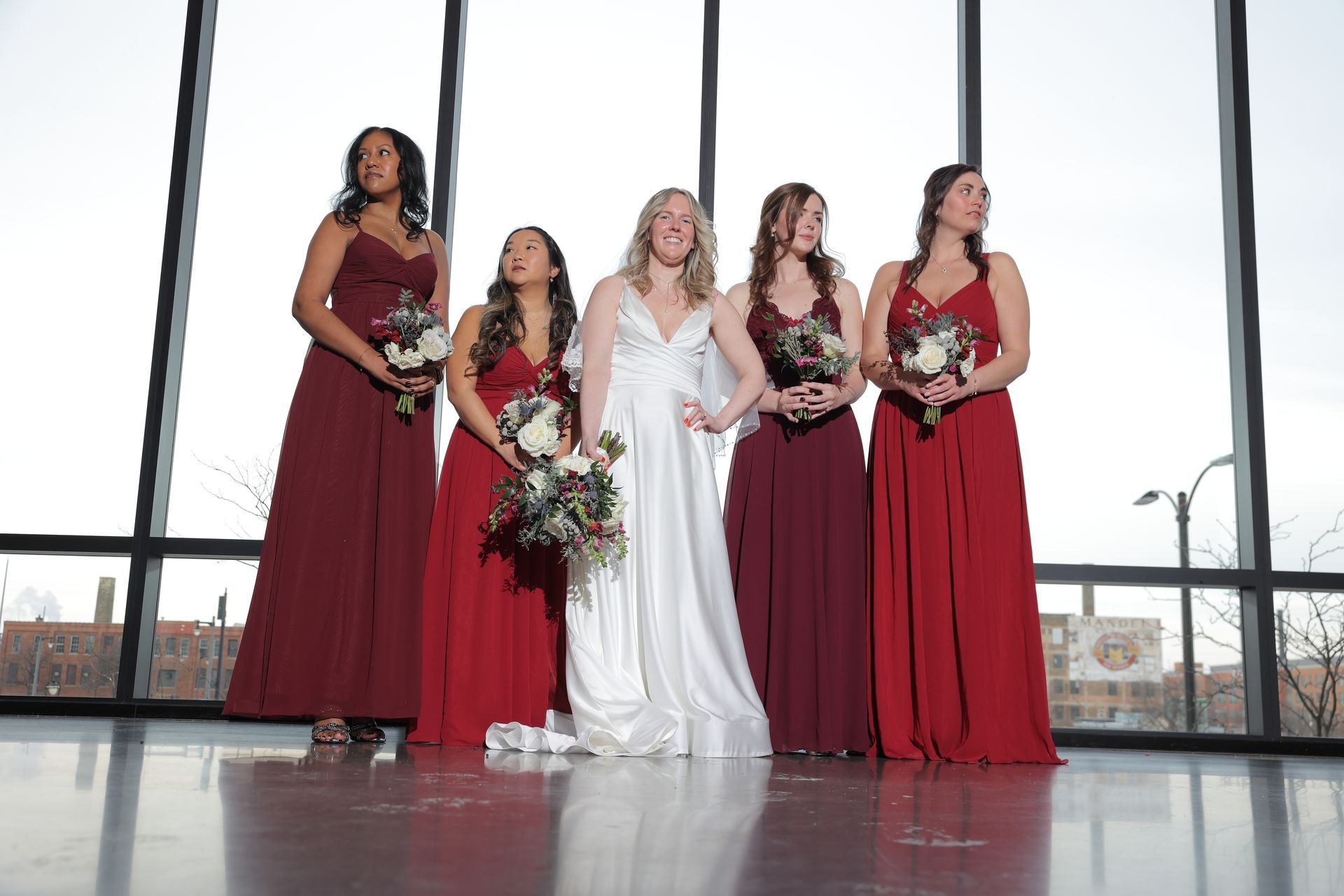 Bride with four bridesmaids in red dresses, holding bouquets, near windows. With Love, Wedding management, Milwaukee Wedding Coordinator