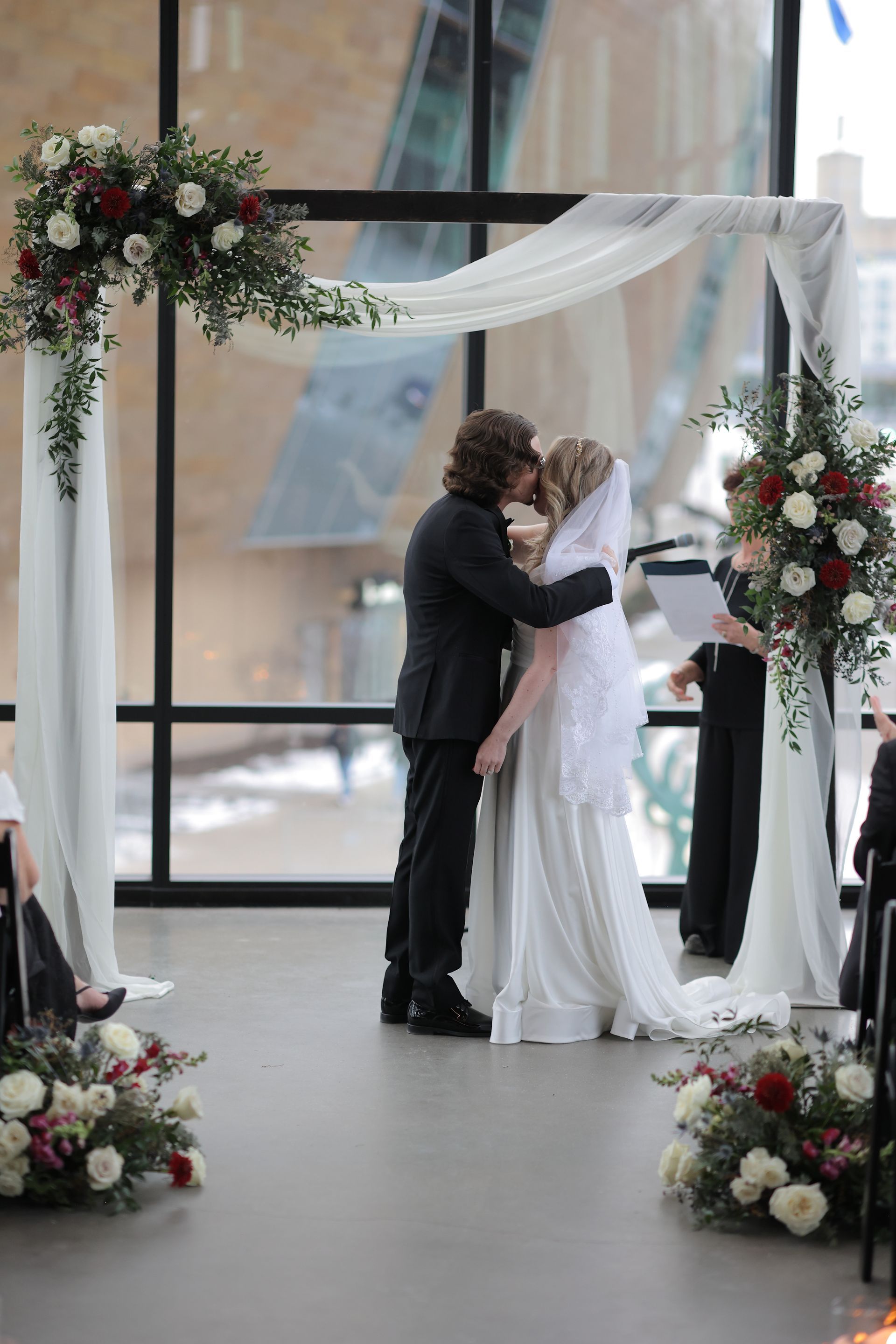 Couple kissing under a floral arch during a wedding ceremony in a modern building.
With Love, Wedding management, Milwaukee Wedding Coordinator