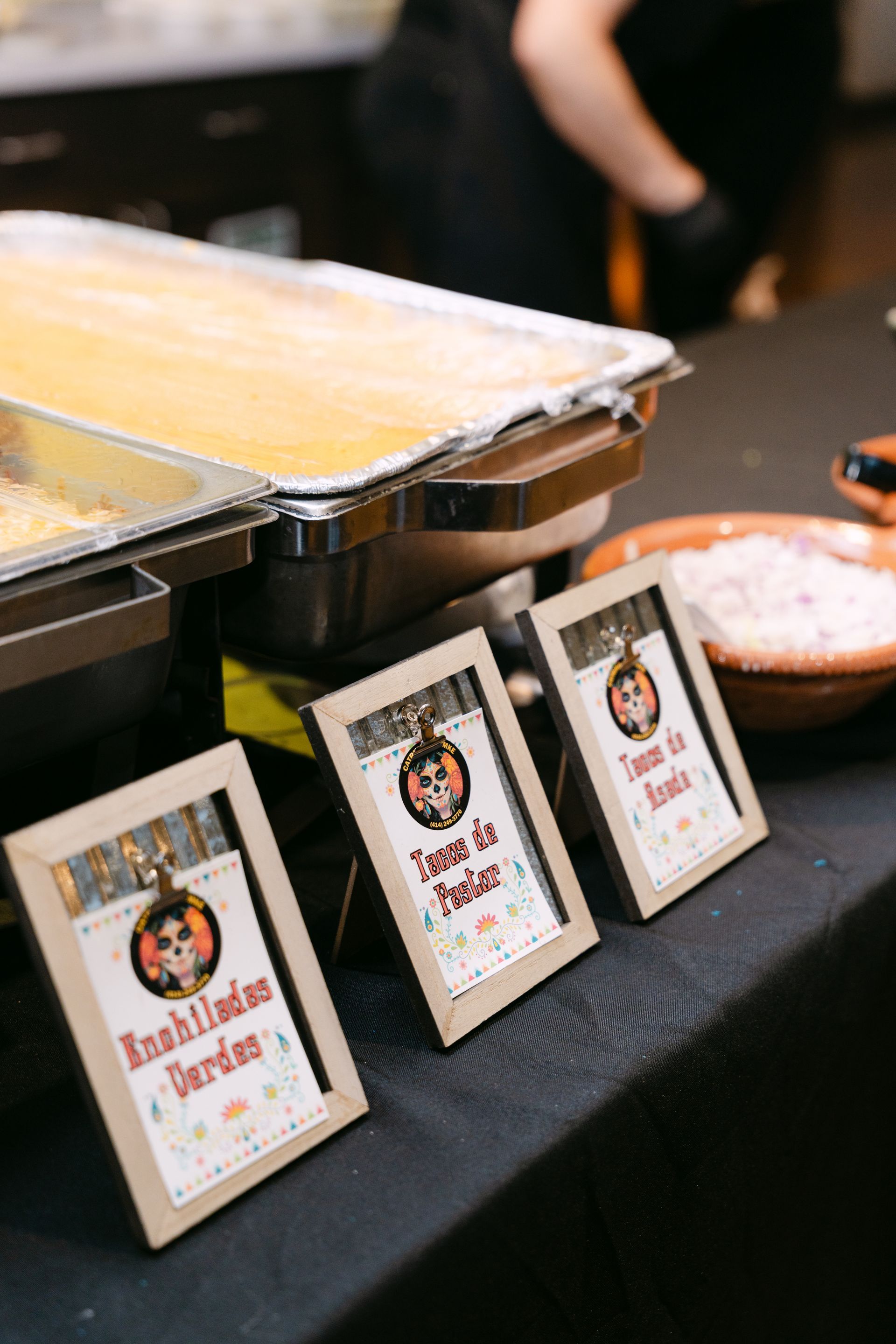 Food buffet with signs for Enchiladas, Tacos, and toppings.