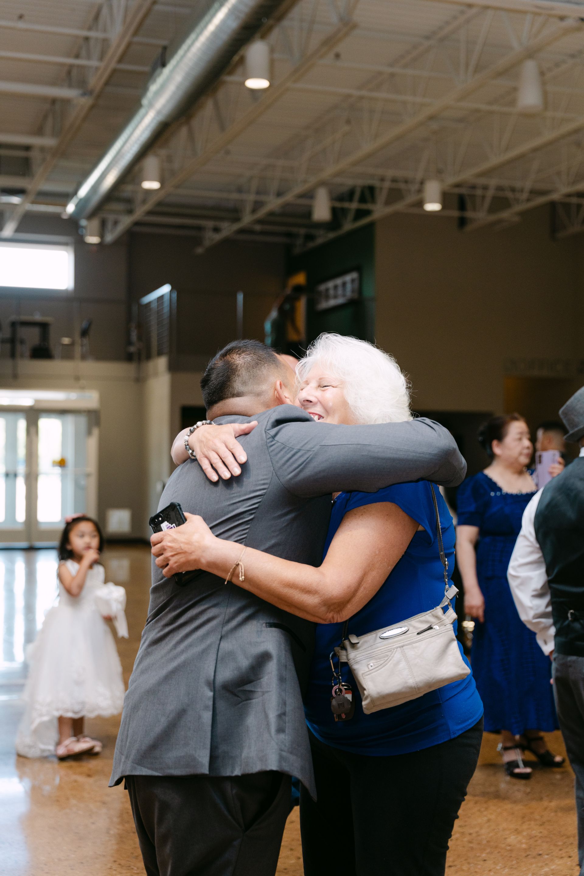 Man in gray suit hugs woman in blue shirt, light-filled room.