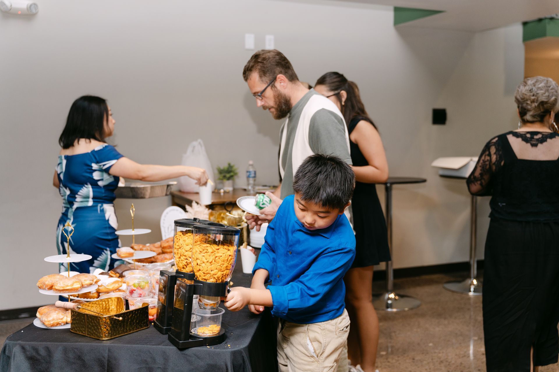 People at a buffet table, one child reaching. Snacks and drinks are on the table.