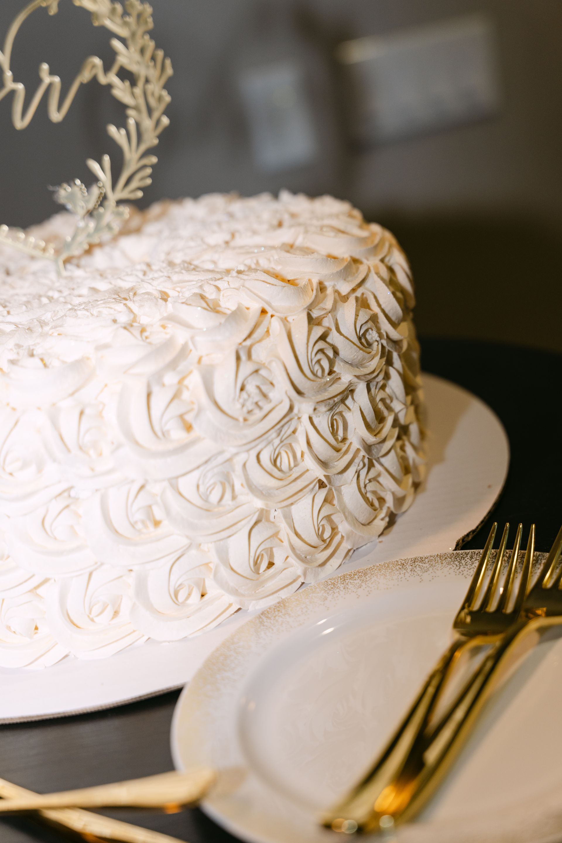 Wedding cake with white frosting and gold accents, atop a plate with gold forks.