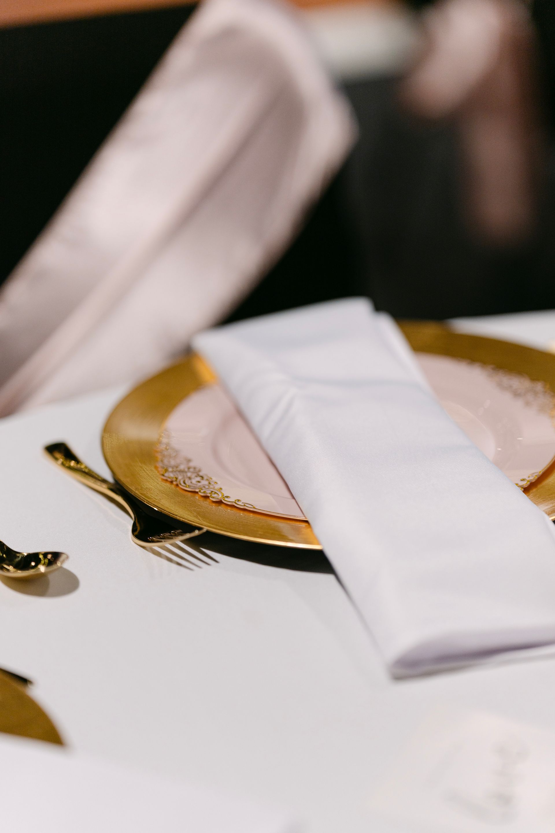 Close-up of a table setting: gold-rimmed plate with a white napkin, gold cutlery.
