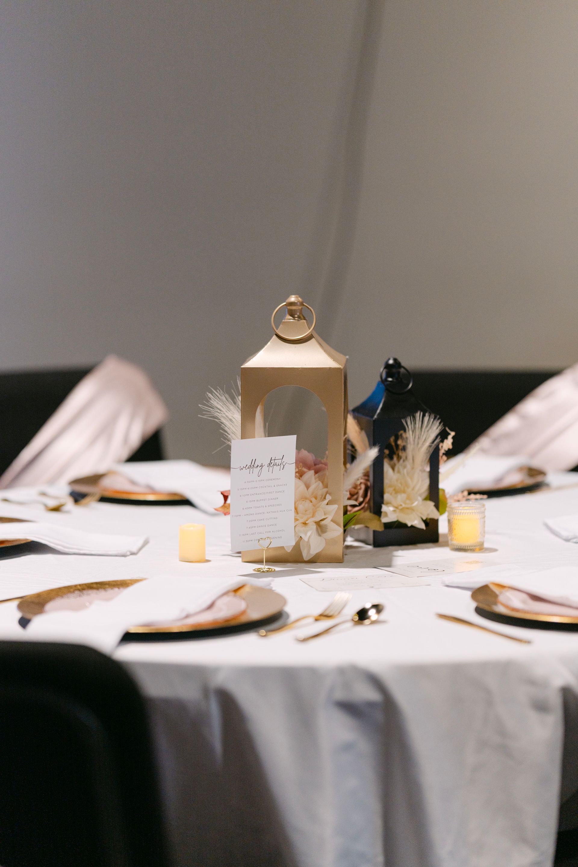 Table setting with gold accents, lanterns, and place cards on a white tablecloth.